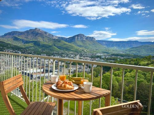 a table with a plate of food on a balcony with mountains at Le Golden View - Vue Imprenable & Parking Gratuit in Chambéry