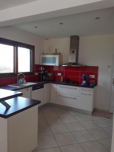 une cuisine avec des placards blancs et un mur rouge dans l'établissement Maison à la campagne proche de l'Océan, à Le Juch