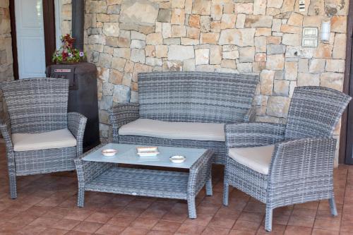 three wicker chairs and a table and a stone wall at I SOGNI DI VENERE in Torre Suda