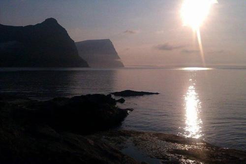 a sun rising over the water with a mountain in the background at Apartment with a panoramic view A in Viðareiði