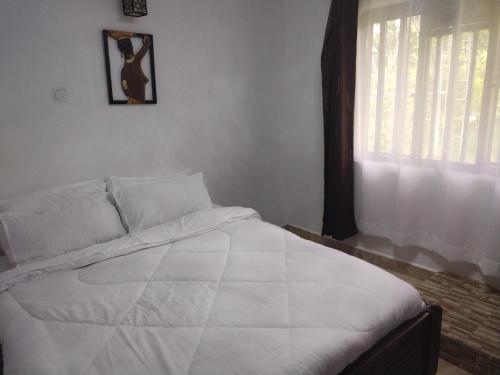 1 cama blanca en un dormitorio con ventana en Precious Home stays, en Maragoli