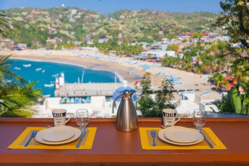 a table with plates and glasses on a table with a view of a beach at Hotel Casa Rush in Puerto Ángel