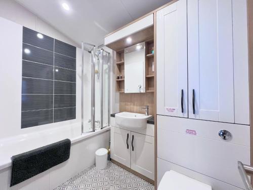 a bathroom with white cabinets and a sink and a tub at Lakeside Dorchester Lodge - Hot Tub with Fishing Peg in Tattershall