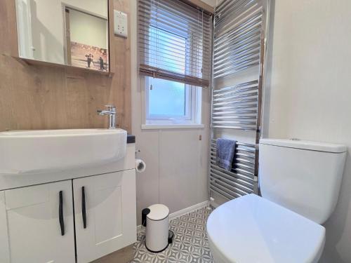 a bathroom with a sink and a toilet and a window at Lakeside Dorchester Lodge - Hot Tub with Fishing Peg in Tattershall