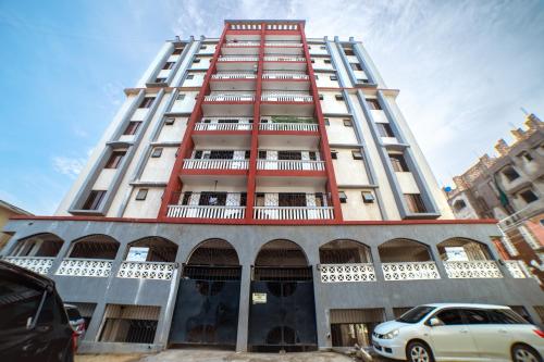 un edificio alto blanco y rojo con coches aparcados delante en JAMAKI Hospitality, en Mombasa