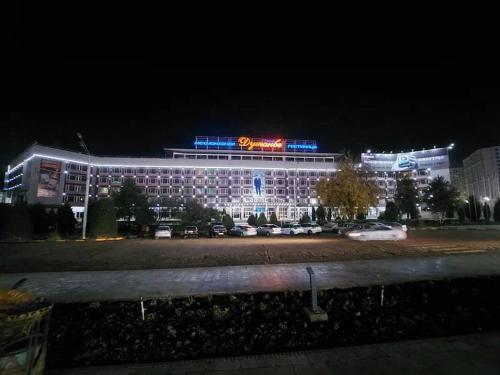 un bâtiment éclairé avec des voitures garées dans un parking dans l'établissement Dushanbe Hotel, à Douchanbé