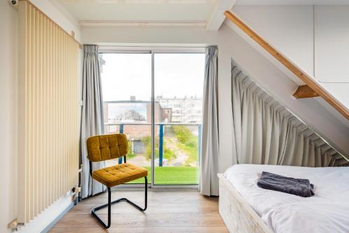 1 dormitorio con 1 cama y 1 silla frente a una ventana en Zon Modern beach house en Bergen aan Zee