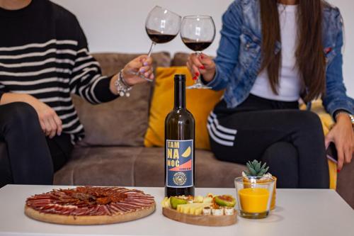 two people holding glasses of wine and a pizza on a table at Apartman Bahus in Zlatibor