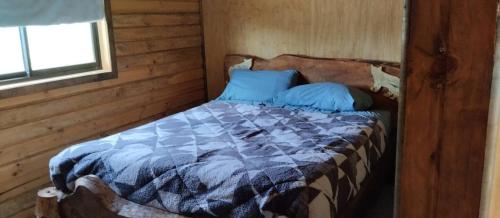 1 cama con almohadas azules en una habitación de madera en El Vacio Fertil, en Lebu