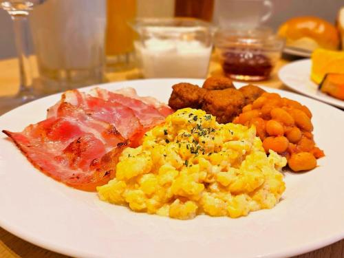 a white plate of food with eggs meat and potatoes at APA Hotel Higashi Shinjuku Kabukicho Higashi in Tokyo