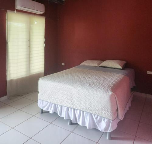 ein Schlafzimmer mit einem weißen Bett in einer roten Wand in der Unterkunft Aparta Hotel Palmerola in Comayagua