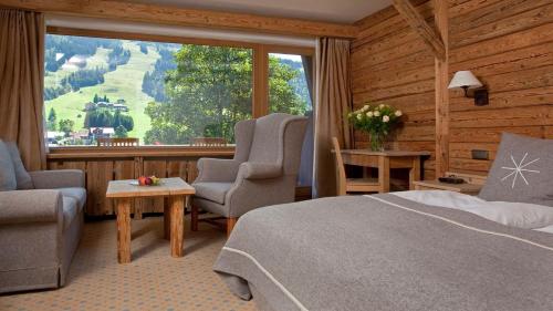 a bedroom with a bed and chairs and a large window at LANIG Hotel Resort&Spa - Wellness und Feinschmeckerhotel - family owned and managed in Oberjoch