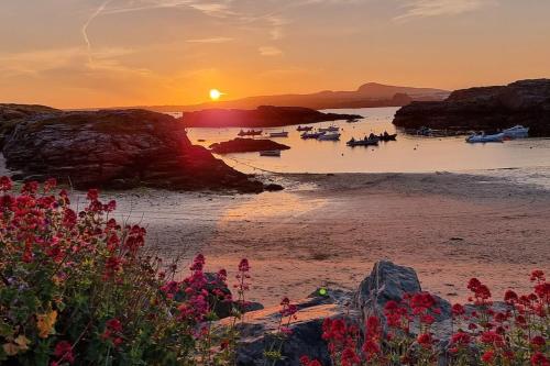 a sunset on a beach with boats in the water at Morlun, Trearddur Bay, Isle of Anglesey in Trearddur