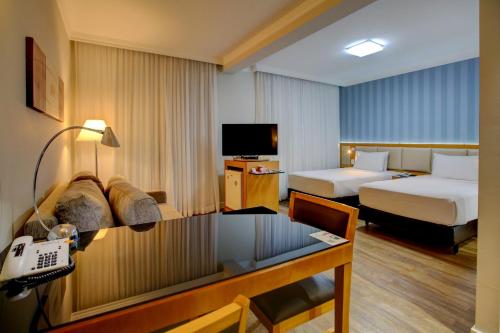 a hotel room with two beds and a desk at Quality Suítes Oscar Freire in Sao Paulo