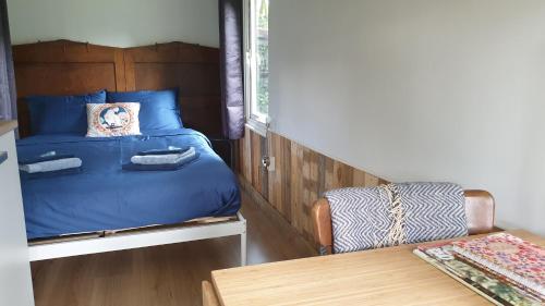 a small bedroom with a blue bed and a table at Pipowagen Bed bij Bos in Putten