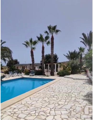 a swimming pool with palm trees and a house at Alojamiento PlayaArco in Los Escullos