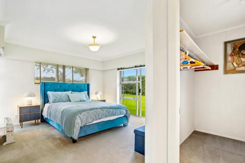 een slaapkamer met een blauw bed en een raam bij Tui Country Retreat with Wi-Fi and Garden Views in Karaka
