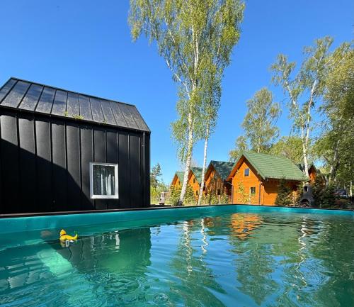 a swimming pool with a black house and a yellow house at Domy nad morzem- Family Resort - Chata Pirata 2 in Dziwnów