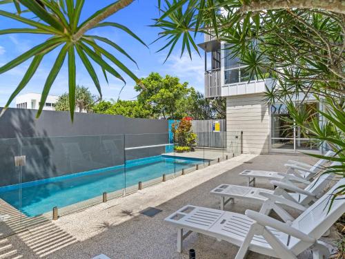a pool with white lounge chairs in front of a building at Ayana Casuarina in Casuarina