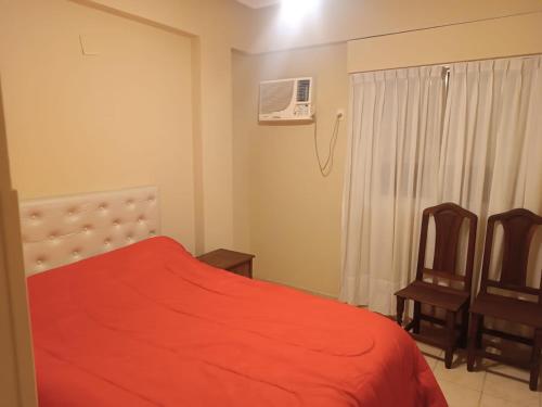 1 dormitorio con 1 cama roja y 2 sillas en Las Heras 361 en San Miguel de Tucumán