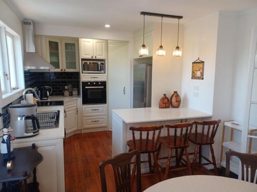 a kitchen with white cabinets and a island with bar chairs at cosy home in New Lynn in Auckland