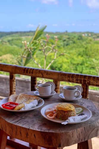 ein Holztisch mit zwei Tellern mit Essen und Kaffeetassen in der Unterkunft D Sebuluh Bungalow in Nusa Penida