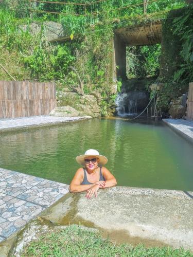 mężczyzna w kapeluszu siedzący w basenie z wodą w obiekcie Pousada Iasbeck w mieście Santa Rita de Jacutinga