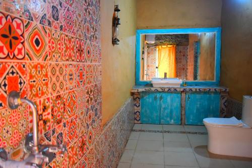 y baño con pared de baldosa, lavabo y espejo. en Dirghayu Bhava Retreat, en Dehradun