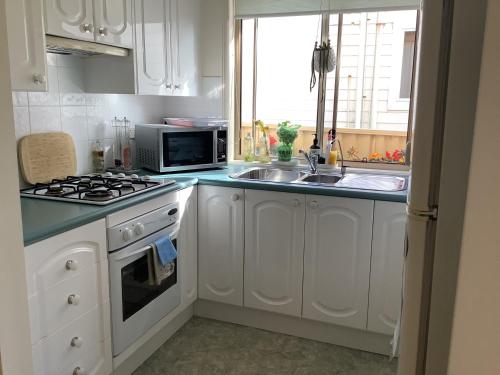 a kitchen with white cabinets and a sink and a microwave at Maggie's Nest-Come & Rest in Killarney Vale