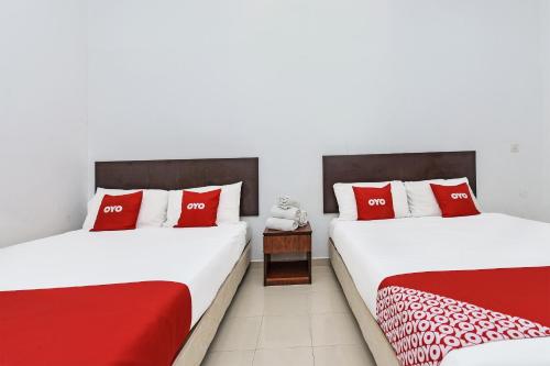 2 łóżka w pokoju z biało-czerwonymi poduszkami w obiekcie OYO 275 Senyum Inn w mieście Pantai Cenang