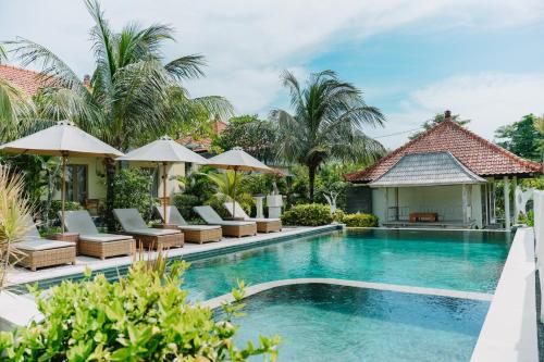 a pool at a resort with chairs and umbrellas at Taman Asih Bingin Homestay in Uluwatu
