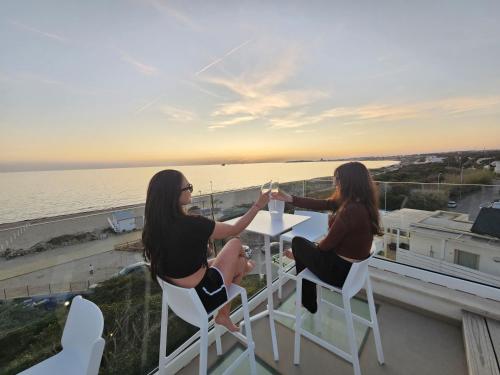 two women sitting at a table on a balcony with the ocean at Villa Dune Luxury Roof Top Pool Wellness in Gallipoli