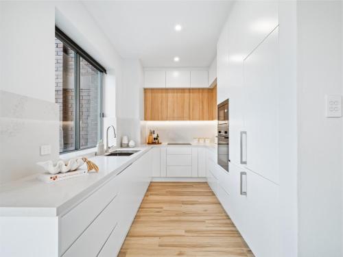 a kitchen with white cabinets and a wooden floor at Peach at Palm View Collective in Sydney