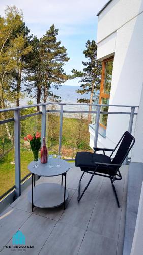 a chair and a table on a porch with a view of the ocean at Pod Brzozami Apartamenty Let's Sea Gąski in Gąski