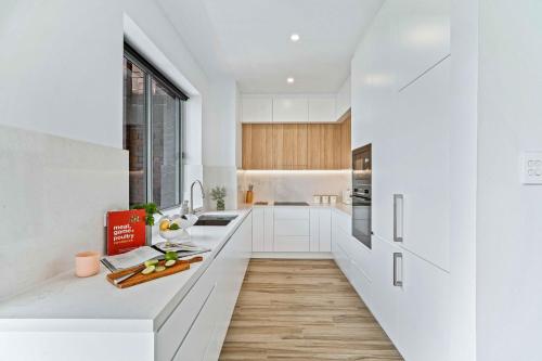 a white kitchen with white cabinets and a counter at Phoenix at Palm View Collective in Sydney
