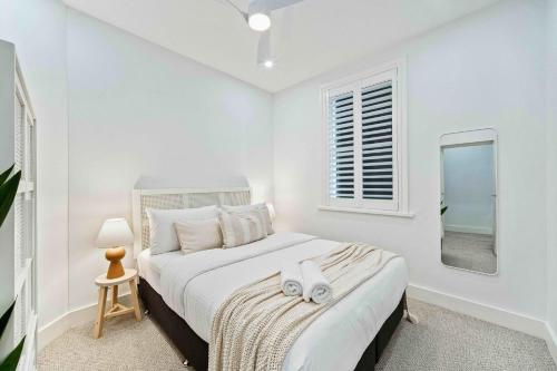 a white bedroom with a bed and a mirror at Phoenix at Palm View Collective in Sydney