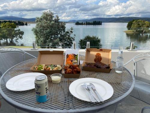 a table with a plate of food on a table near the water at Horizons 424 Lake Jindabyne Waterfront 2 Bedroom Apartment in Jindabyne