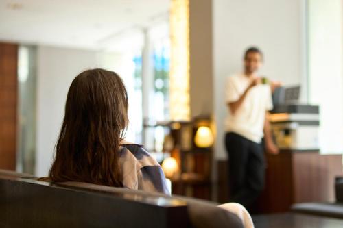 a woman sitting in a chair watching a man at Hotel Resol Trinity Kanazawa in Kanazawa