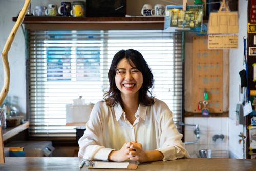 a woman sitting at a table in a kitchen at Kobe Guesthouse MAYA in Kobe