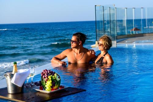 um homem e uma mulher numa piscina ao lado do oceano em Alexander Beach Hotel & Village Resort em Mália