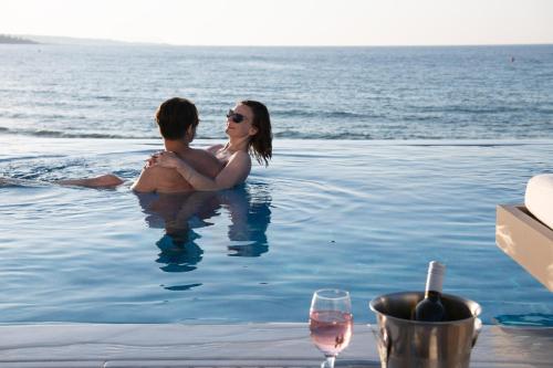 un homme et une femme assis dans une piscine dans l'établissement Alexander Beach Hotel & Village Resort, à Mália