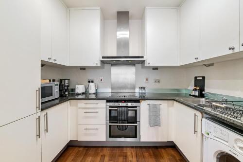 a kitchen with white cabinets and stainless steel appliances at Londwell, Canary Wharf River Thames Balcony Suite in London