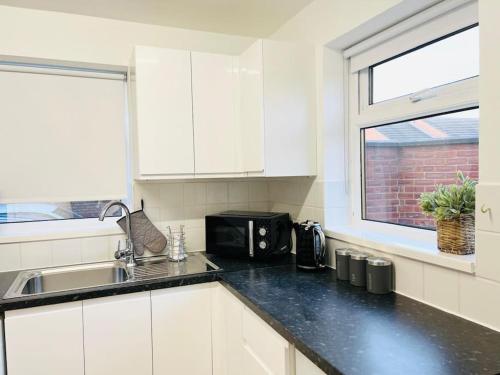 a white kitchen with a sink and a microwave at New fully furnished cosy home in Balderton
