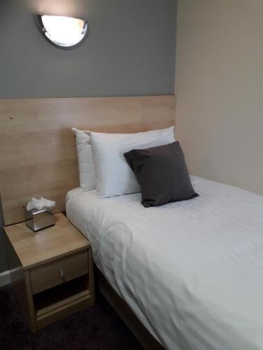 a bed with a pillow on it next to a night stand at Cambridge Hotel Waterfront in Brighouse