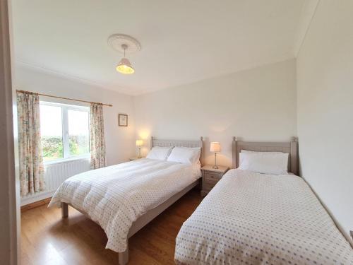 deux lits dans une chambre blanche avec une fenêtre dans l'établissement Foregloss Cottage, à Ballyconneely