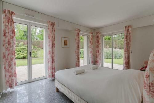 a bedroom with a large bed and large windows at Luxury haven with swimming pool and tennis court Deauville in Deauville