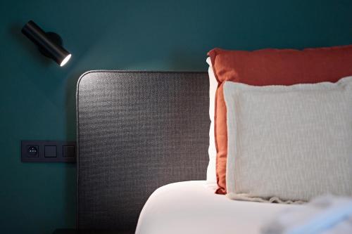 a bed with an orange and white pillow next to a wall at Hotel La Malle Poste in Rochefort