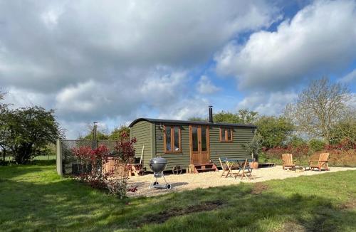 a green tiny house with a grill and chairs at Hidden Gem Luxury Shepherd Hut - Pea Pod in Wimbish