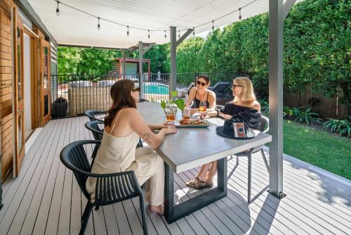 three women sitting at a table on a deck at Battery Hill Pet-Friendly Poolside Paradise in Caloundra