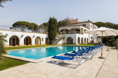 a pool with chairs and an umbrella and a house at Villa Maricel in Sant Feliu de Guixols